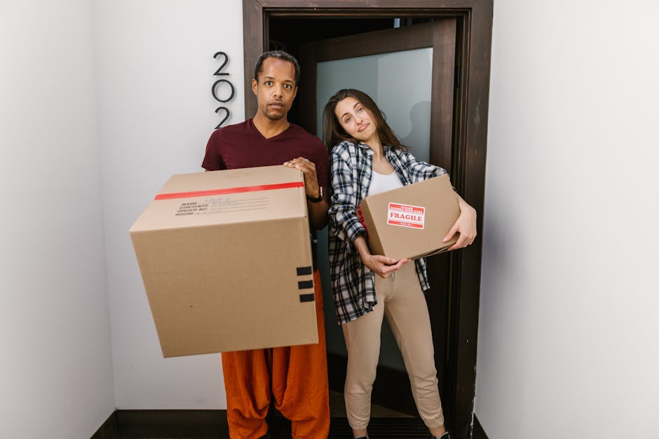 Inside a property during a home relocation process, a professional removals team at [COMPANY_NAME] is seen loading furniture and cardboard boxes into a large white van parked outside on a paved drivew