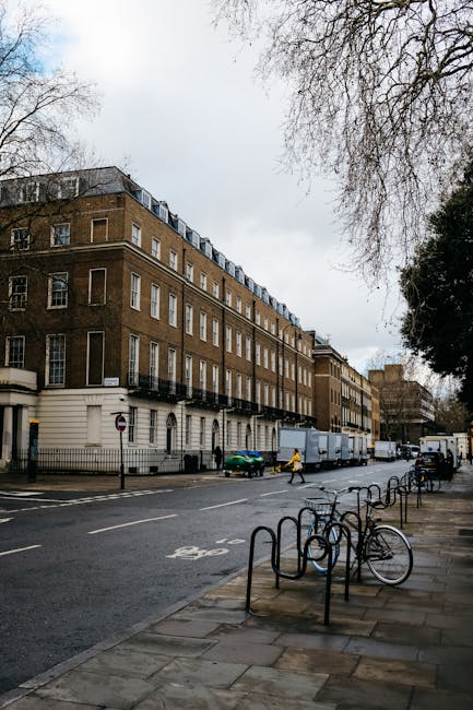 The image shows a row of elegant, white Victorian-style terraced houses with detailed architectural features such as arched windows, decorative columns, and wrought iron balconies, situated along a bu